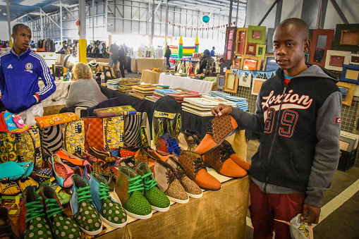 Johannesburg , South Africa - October 02 , 2017: man holding he,s self made shoes, in vivid colors.Market is  in the backround,young designers take to markets to expose their designs to new clients.This is a trend of start ups in a shaky business climate