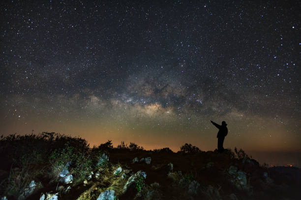 istock A Man is standing next to the milky way galaxy pointing on a bright star at Doi Luang Chiang Dao with Thai Language top point signs. Long exposure photograph.With grain 857720222
