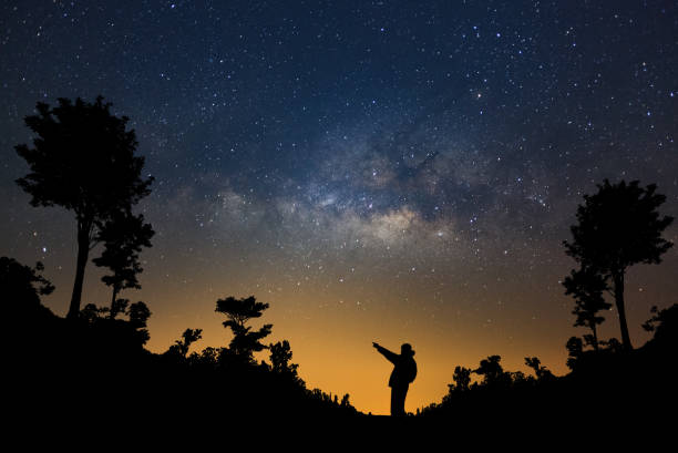 istock A Man is standing next to the milky way galaxy pointing on a bright star in forest, Long exposure photograph, with grain. 857720300