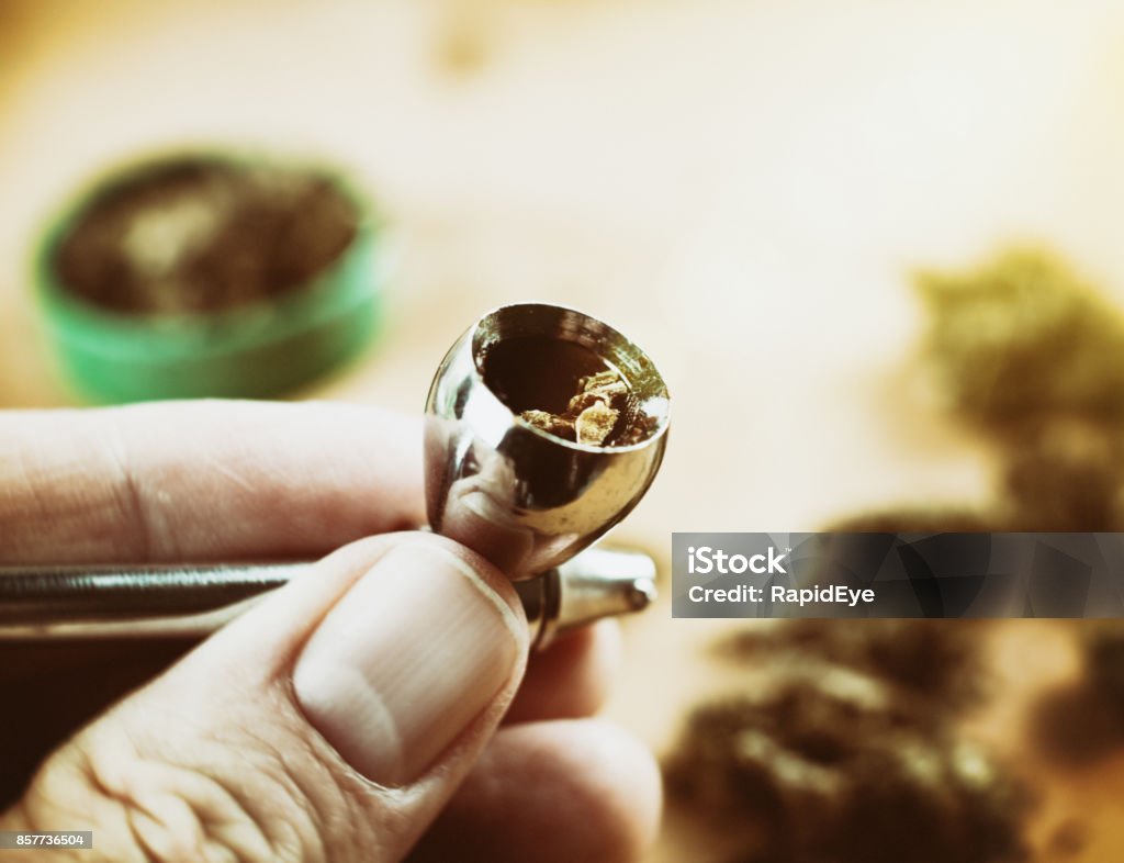 Hand holding dope pipe filled with cannabis A man's hand holds a filled cannabis pipe. Bong Stock Photo