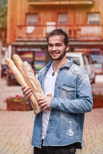 Young man with several poles of fresh baguette in the arm on the street.