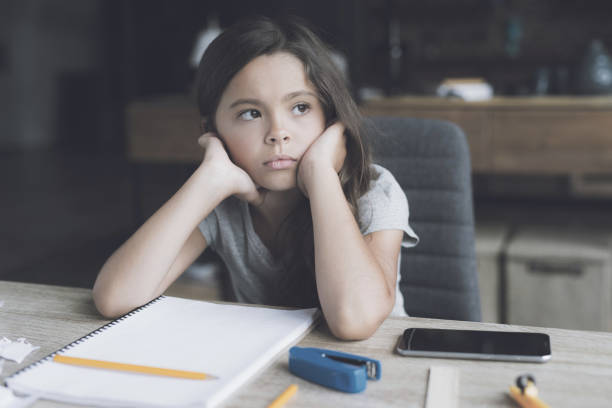 istock The dark-haired girl sits at her desk with a bored expression. Next to it is a white notebook and her smartphone 857769250