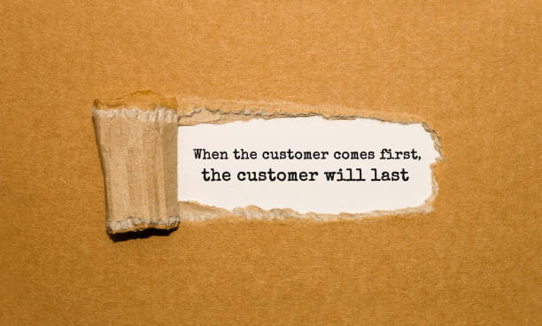 The text When the customer comes first the customer will last appearing behind torn brown paper stock photo