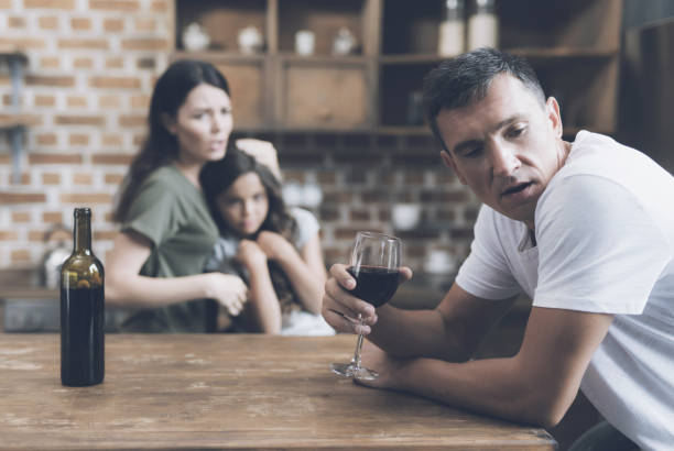 mężczyzna ze wstydu odwraca się od żony i córki, którzy nagannie patrzą na niego, gdy pije - table on wine alcoholism zdjęcia i obrazy z banku zdjęć