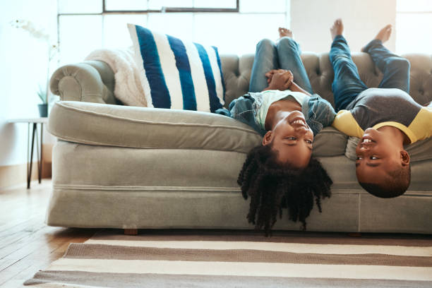 Upside down but doing the right type of fun Shot of a brother and sister hanging upside down off the sofa at home sibling stock pictures, royalty-free photos & images