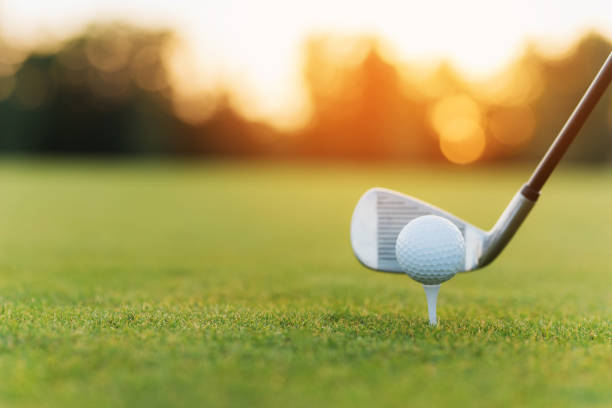 el club de golf detrás de la pelota de golf en el stand. contra el fondo de la hierba y puesta de sol - golf club golf golf course equipment fotografías e imágenes de stock