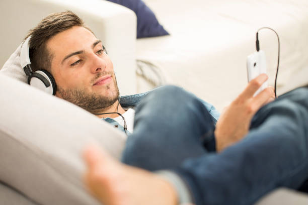 istock Man relaxing in sofa with smartphone and headphones 857802520