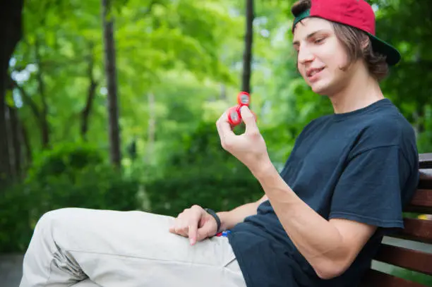 Hipster in a cap sits on a bench and spins a fidget-spinner