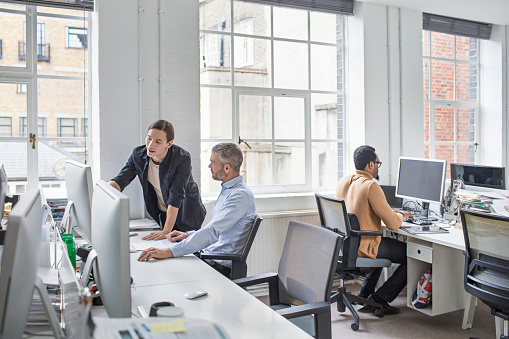 Creative businessmen discussing over computer at desk. Multi-ethnic business professionals are working in new office. They are wearing smart casuals.