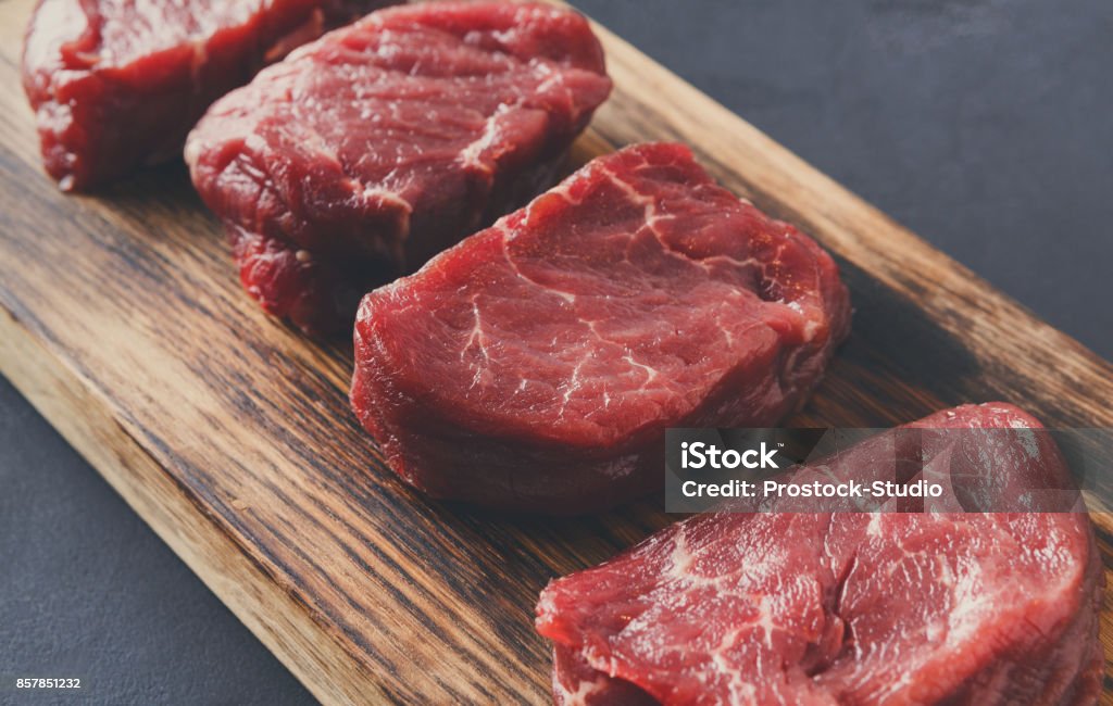 Raw beef filet mignon steaks on wooden board at gray background Raw filet mignon steaks. Slices of fresh beef meat arranged in a row on wooden cutting board at gray background with copy space. Organic ingredients for restaurant meals, meat texture closeup Meat Stock Photo