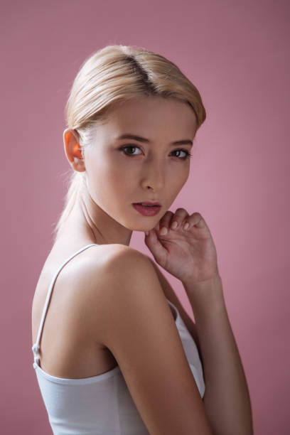 troskliwa blondynka dotykająca jej podbródka - vertical studio shot indoors pink zdjęcia i obrazy z banku zdjęć