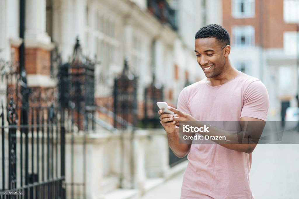 Handsome black guy in London, using mobile phone Portrait of handsome young man in London using phone for text messaging Men Stock Photo