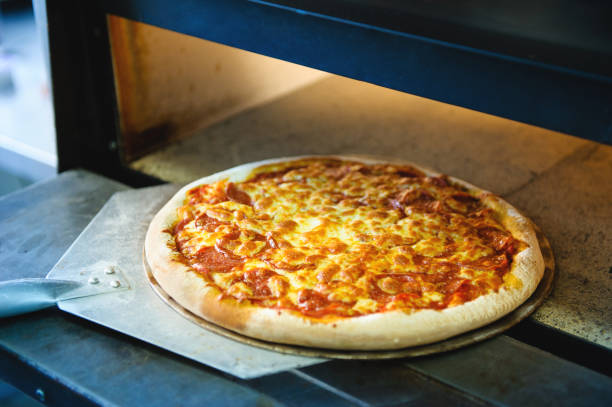 photo gorizontal Pizza with cheese on a metal pan for baking in an electric oven