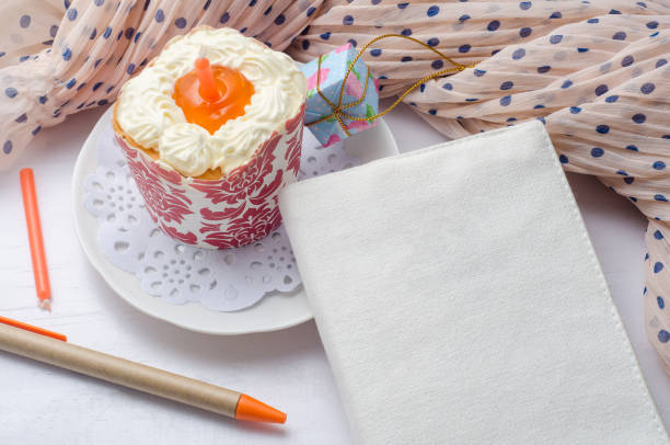 Blank notebook with pen and cupcake on wooden table.