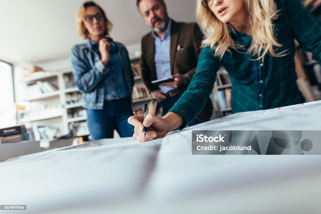 Team of architects working on construction plan Team of architects working on construction plan. Designers working on blueprint on table in office. Focus on female hand pointing on drawing. Architect Stock Photo