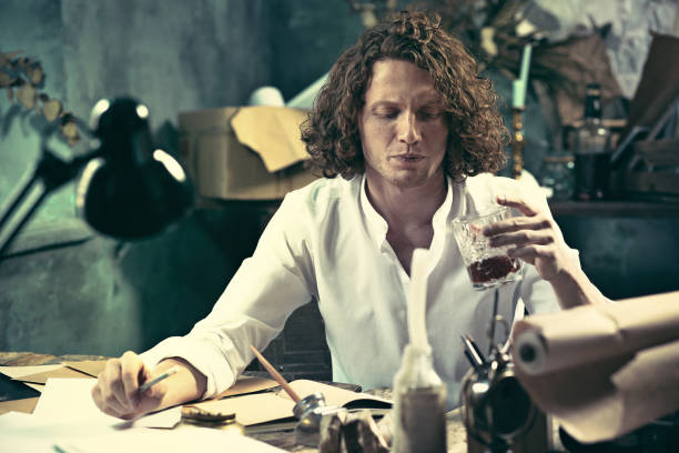 istock Writer at work. Handsome young writer sitting at the table and writing something in his sketchpad 857897514