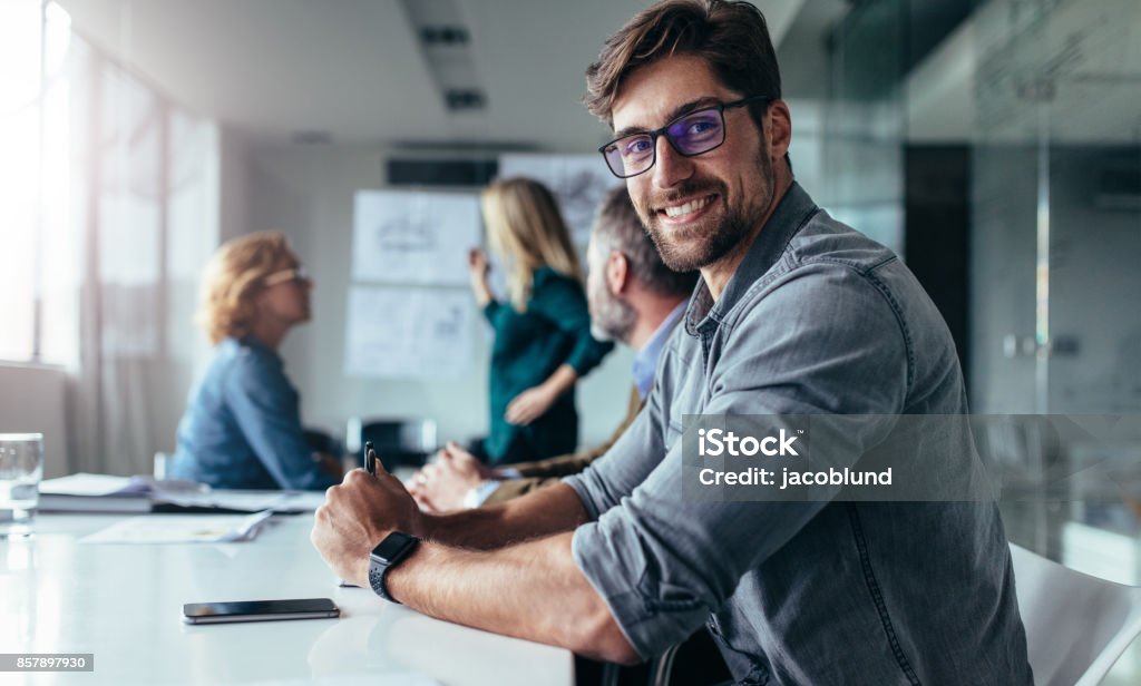 Businessman sitting in board room during presentation Horizontal shot of young man sitting in meeting room. Businessman sitting in board room during new project discussion. Business Stock Photo