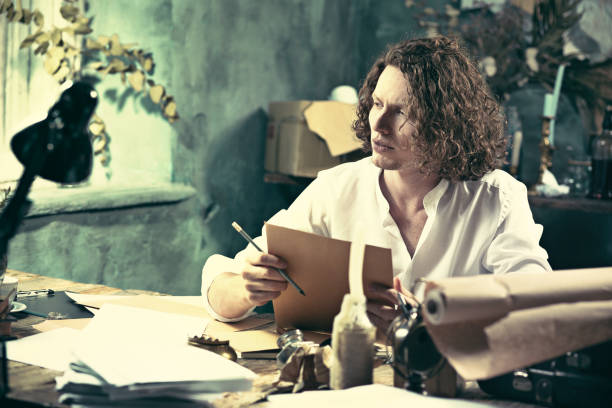 istock Writer at work. Handsome young writer sitting at the table and writing something in his sketchpad 857898172