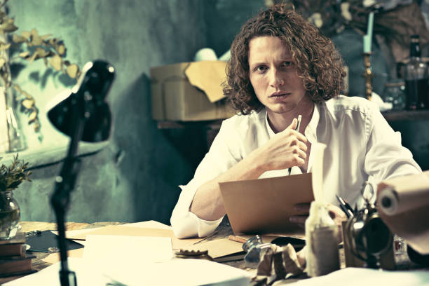 istock Writer at work. Handsome young writer sitting at the table and writing something in his sketchpad 857900286
