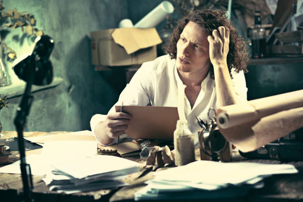 istock Writer at work. Handsome young writer sitting at the table and writing something in his sketchpad 857900770