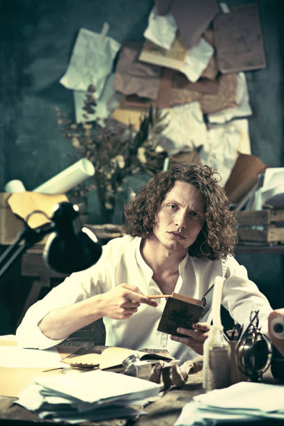 istock Writer at work. Handsome young writer sitting at the table and writing something in his sketchpad 857901896
