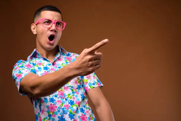 Photo of Studio shot of young multi-ethnic Asian tourist man against colored background