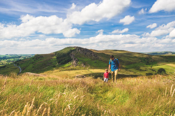 Father and Son Hiking in Peak District A father and his young son hike up a hill at The Roaches, Peak District National Park, Derbyshire, United Kingdom. The father is spending some quality bonding time with his son and showing him the beauty of England on a summer afternoon. derbyshire photos stock pictures, royalty-free photos & images