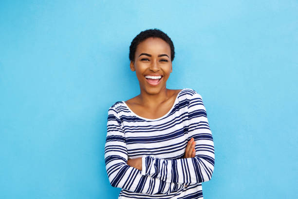 happy young black woman laughing against blue wall - fashion women posing looking at camera imagens e fotografias de stock