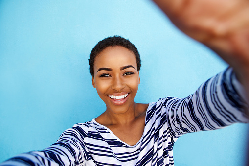 Close up portrait of smiling african american woman taking selfie against blue wall