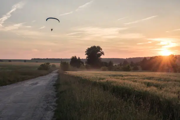 summer evening at sunset time in countryside with fields along rural road and moody sky with paraglider/paraglider position change