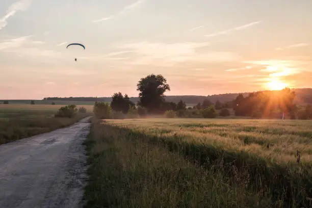 summer evening at sunset time in countryside with fields along rural road and moody sky with paraglider/paraglider position change