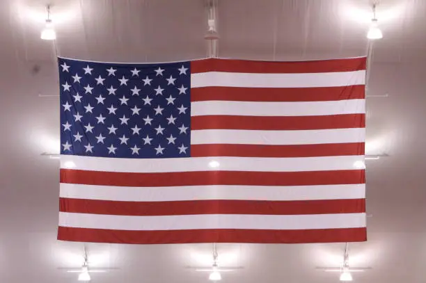 an american flag hangs in the rafters of a stadium backlit by the stadium lighting