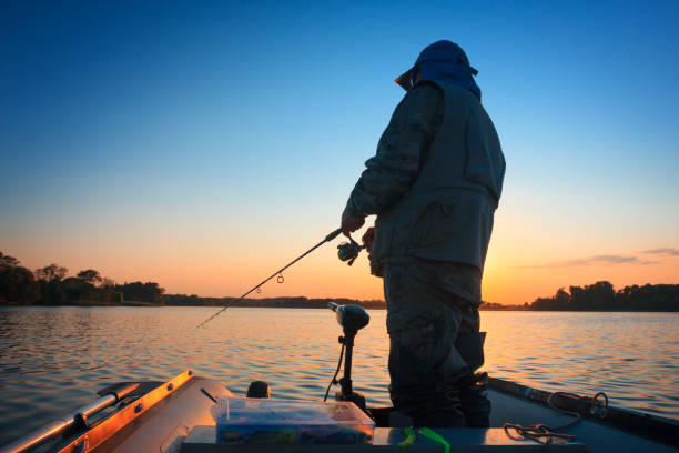 un pescador pescando en un lago al atardecer - bass fotografías e imágenes de stock