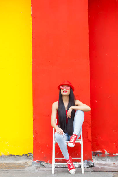 Woman wearing pink vest, blue headphones and holding blue can in front of yellow and blue wall background