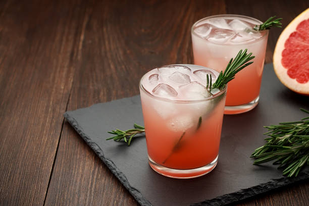 Two glasses of citrus summer drink with grapefruit and rosemary on dark background. stock photo