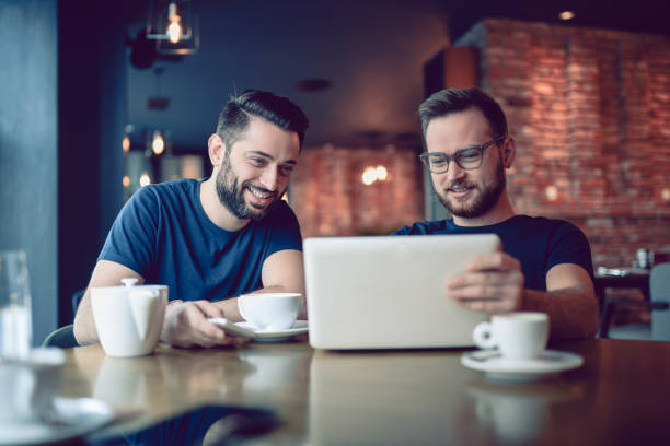 istock Two Smiling  Male Freelancers Drinking Coffee and Video Conferencing In Cafe Restaurant 857995986