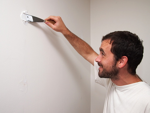Man preparing a wall for painting.  The black hair caucasian man is fixing a hole in the wall.