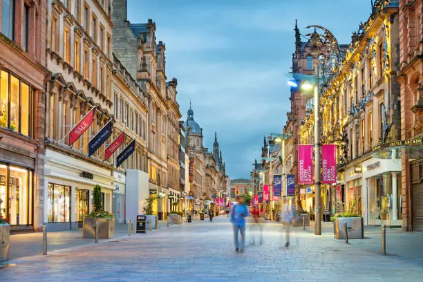Stock photograph of people walking on Buchanan Street in downtown Glasgow, Scotland, UK at twilight. Buchanan Street forms the central stretch of Glasgow's famous shopping district.