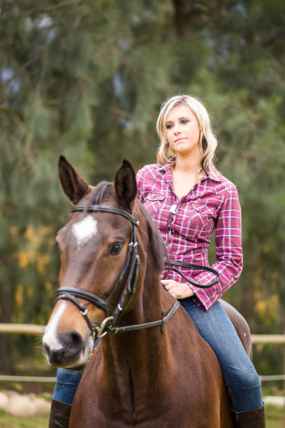 Sexy blond farm girl riding her horse on a farm in South Africa Beautiful elegance blonde woman cowgirl, riding a horse. Clothed leg in blue jeans, brown leather jacket, boots. Has slim sport body. Portrait nature. People and animals. Equestrian. Close up checkered cowboy boots stock pictures, royalty-free photos & images