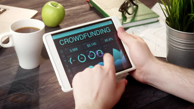 Monitoring crowdfunding data using tablet computer at desk