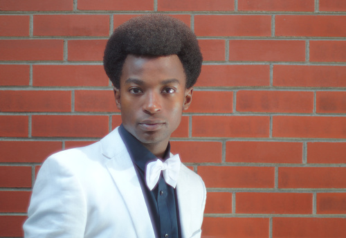 young man wearing bow tie and black shirt white jacket on brick wall background