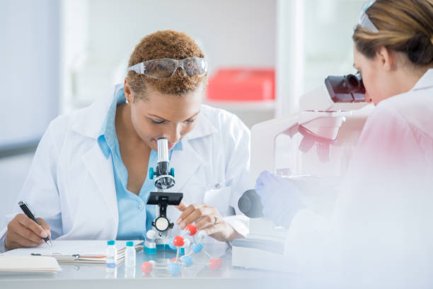 istock Mid adult female lab technician focuses on simple microscope image 858045852