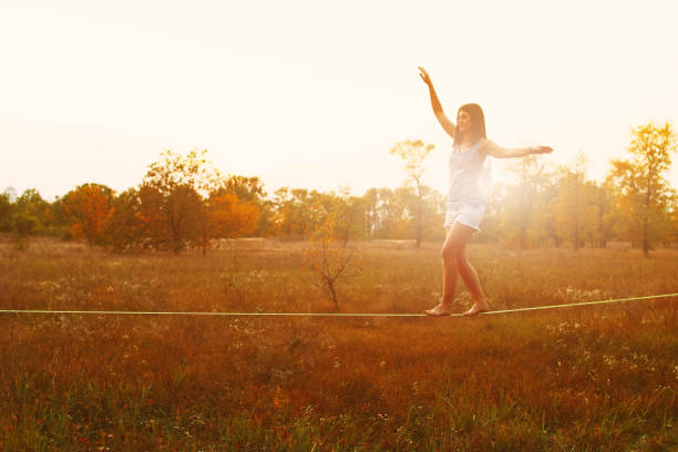 Woman walking on slackline in the meadow at sunset.