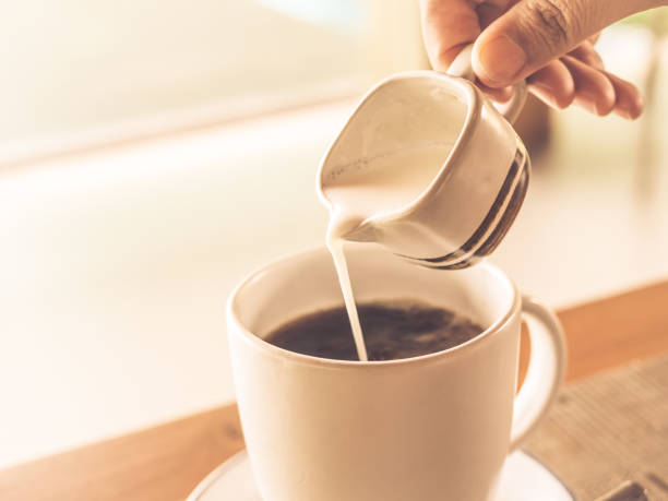 istock Closeup woman hand  pouring hot milk into black coffee cup during breakfast time, with selective focus. 858064290