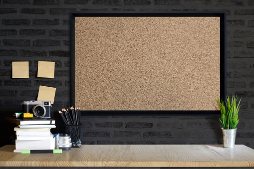 Desk space concept. Mock up Cork board, vintage camera and films on wood table workplace with supplies.