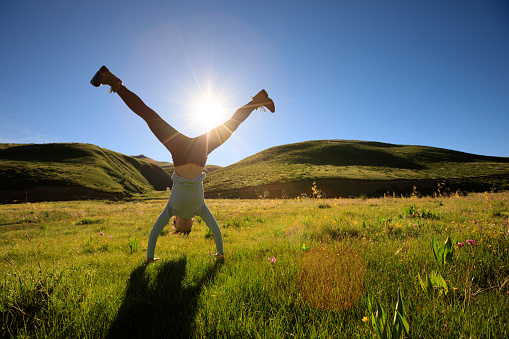 woman doing a handstand in a sunrise meadow