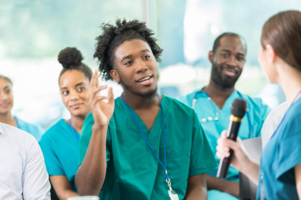 jovem profissional de saúde masculina faz pergunta durante a conferência - male black medical student mature student - fotografias e filmes do acervo