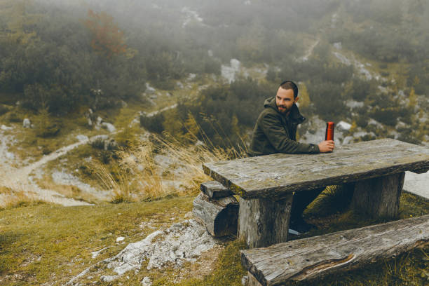 istock Man looking away while sitting on wooden bench with thermo bottle in the hands 858107264