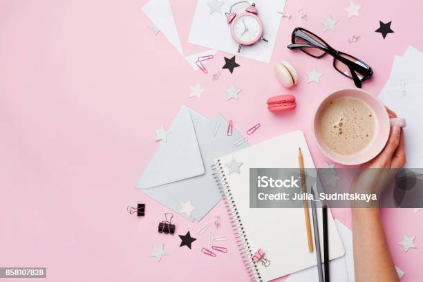 Woman Hand With Cup Of Coffee Macaron Office Supply And Empty Notebook On Pink Pastel Table Top View Fashion Female Blogger Working Desk Stock Photo - Download Image Now