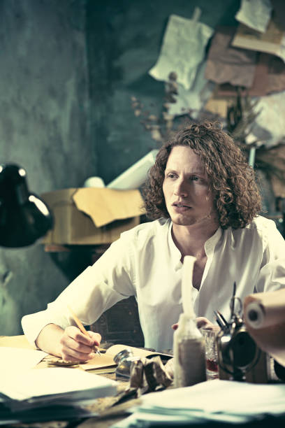 istock Writer at work. Handsome young writer sitting at the table and writing something in his sketchpad 858115028